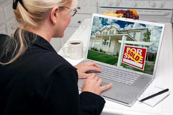 Woman in kitchen using laptop to research real estate. screen can be easily used for your own message or picture. picture on screen is my copyright as well