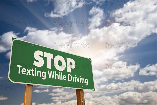 Stop texting while driving green road sign with dramatic sky