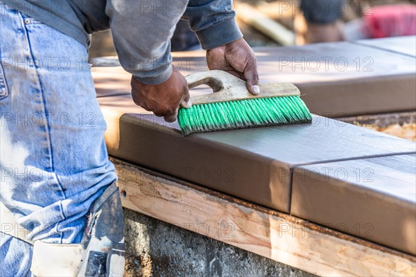 Construction worker using brush on wet cement forming coping around new pool