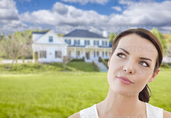 Thoughtful pretty mixed-race woman in front of house looking up and to the side