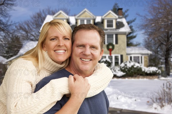 Happy couple in front of beautiful house with snow on the ground