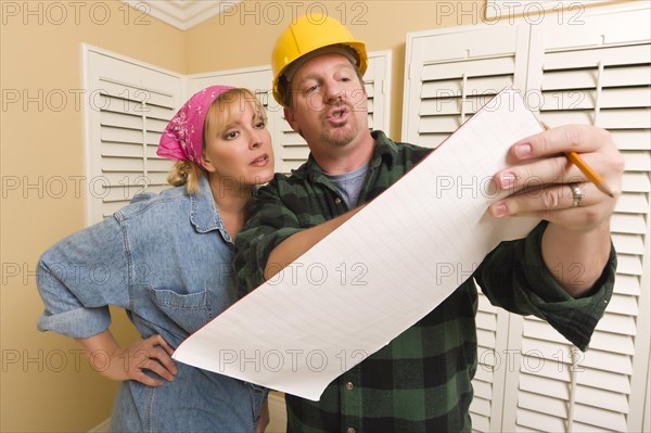 Male contractor in hard hat discussing plans with woman in room