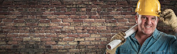 Male contractor in hard hat holding construction plans in front of old brick wall banner with copy space