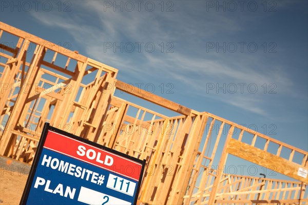 Sold lot real estate sign at new home framing construction site against deep blue sky