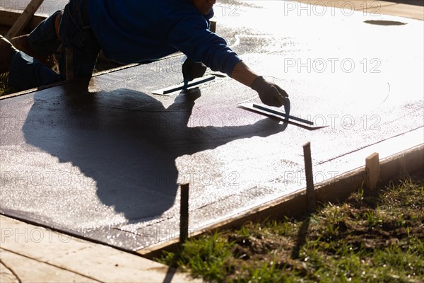 Construction worker smoothing wet cement with trowel tools