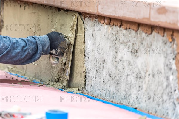 Tile worker applying cement with trowel at pool construction site