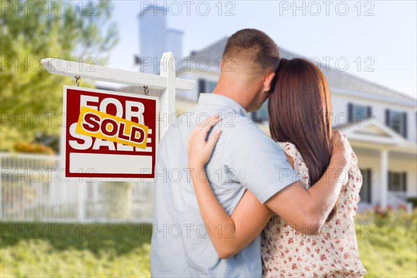 Sold for sale real estate sign and affectionate military couple looking at nice new house