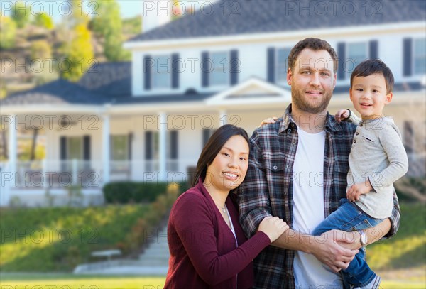 mixed-race chinese and caucasian parents and child in front yard of new custom house