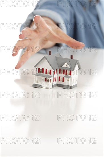 Womans hand reaching for model house on a white surface