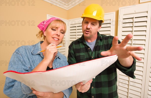 Male contractor in hard hat discussing plans with woman in room