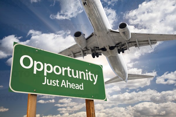 Opportunity green road sign and airplane above with dramatic blue sky and clouds