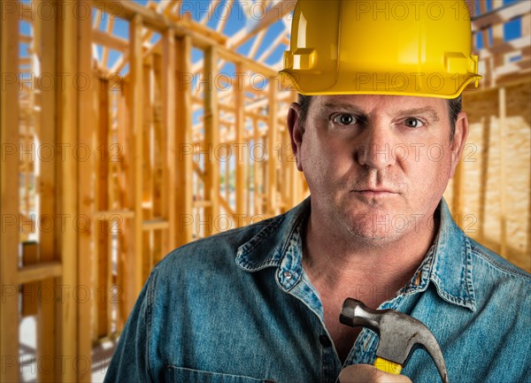 Serious contractor in hard hat holding hammer at construction site