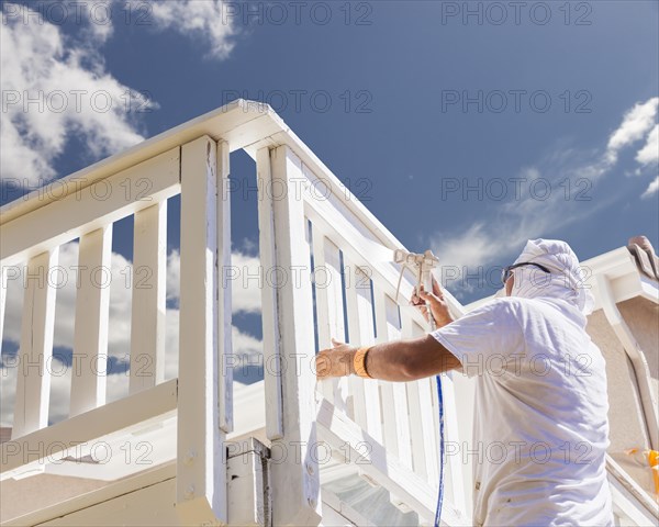 House painter wearing facial protection spray painting A deck of A home