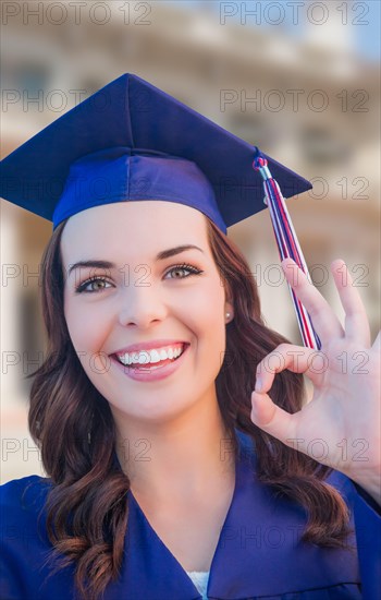 Happy graduating mixed-race woman in cap and gown celebrating on campus