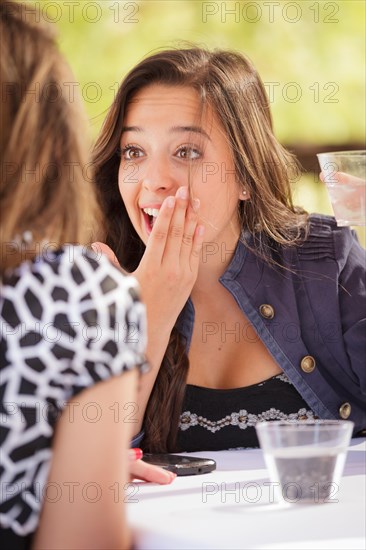 Expressive young adult woman having drinks and talking with her friend outdoors