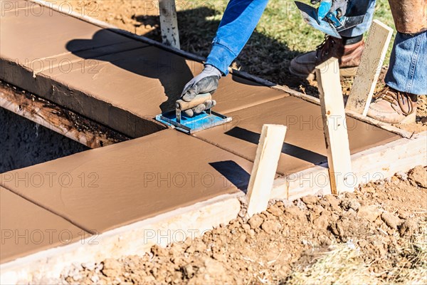 Construction worker using hand groover on wet cement forming coping around new pool