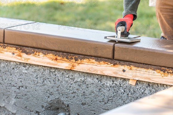 Construction worker using hand groover on wet cement forming coping around new pool