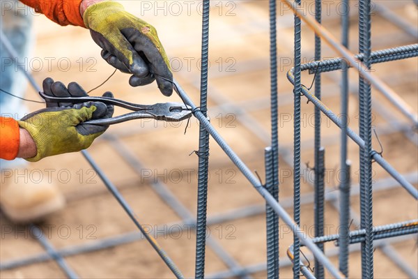 Worker securing steel rebar framing with wire plier cutter tool at construction site