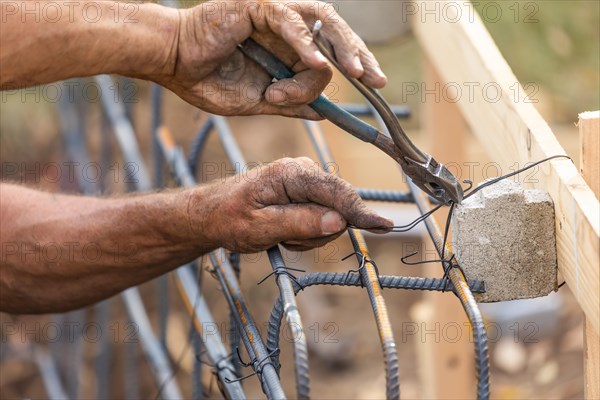 Worker securing steel rebar framing with wire plier cutter tool at construction site