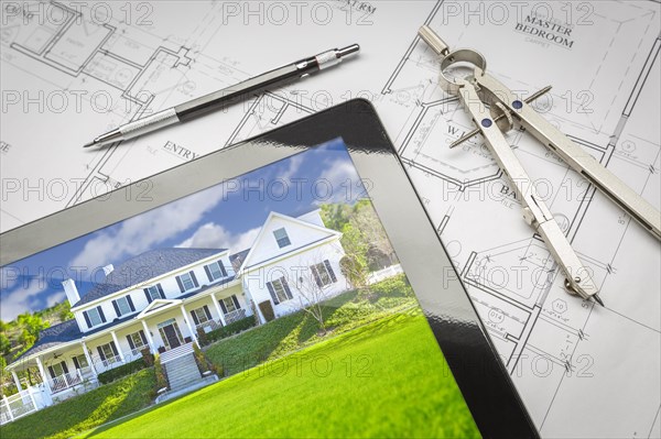 Computer tablet showing finished house sitting on house plans with pencil and compass