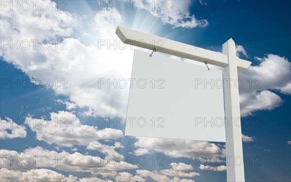 Blank real estate sign over clouds and blue sky with sun rays