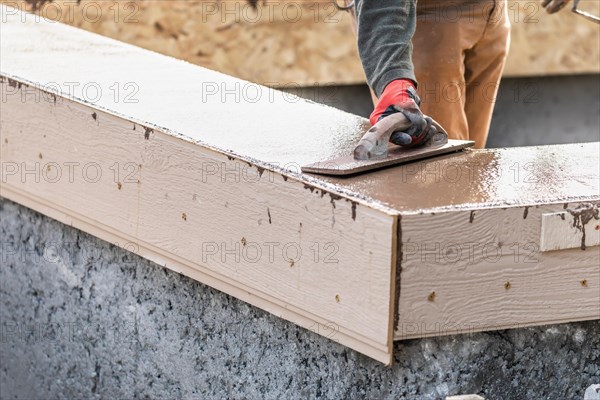 Construction worker using wood trowel on wet cement forming coping around new pool