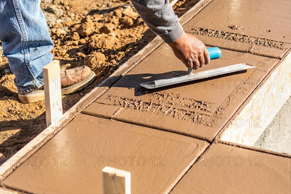 Construction worker using trowel on wet cement forming coping around new pool