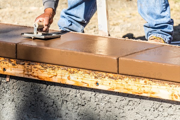 Construction worker using hand groover on wet cement forming coping around new pool