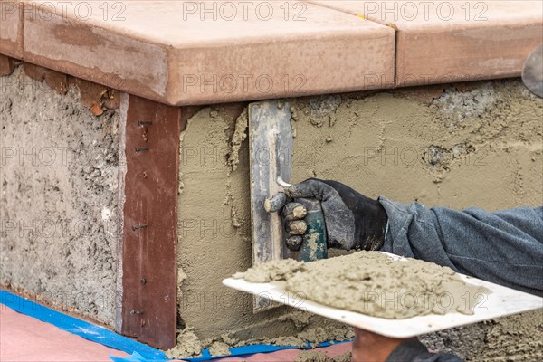 Tile worker applying cement with trowel at pool construction site