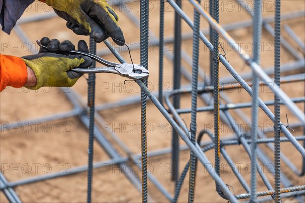 Worker securing steel rebar framing with wire plier cutter tool at construction site