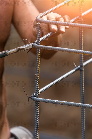 Worker securing steel rebar framing with wire plier cutter tool at construction site