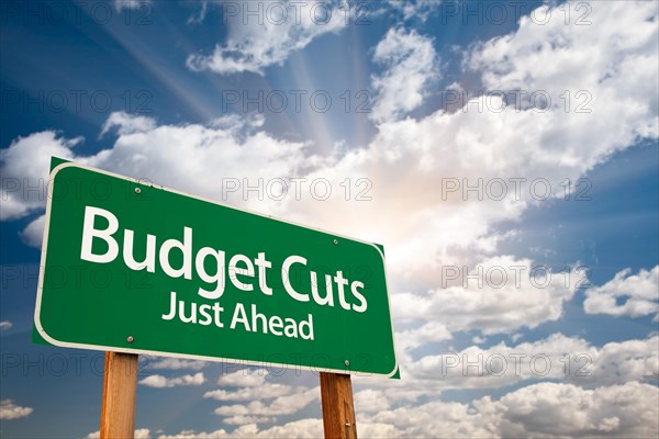 Budget cuts green road sign with dramatic clouds