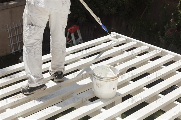 Painter rolling white paint onto the top of A home patio cover