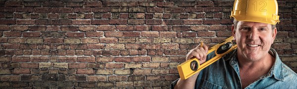 Male contractor in hard hat holding level in front of old brick wall banner with copy space