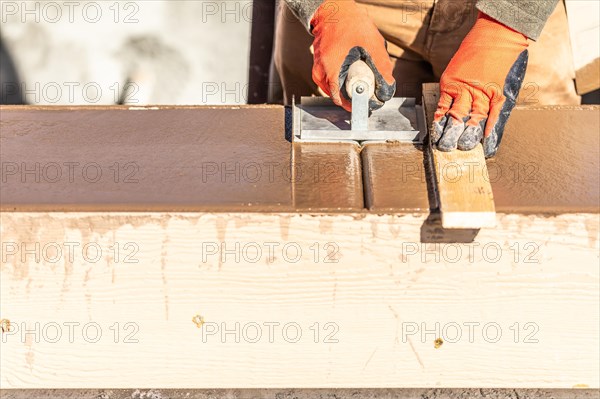 Construction worker using hand groover on wet cement forming coping around new pool