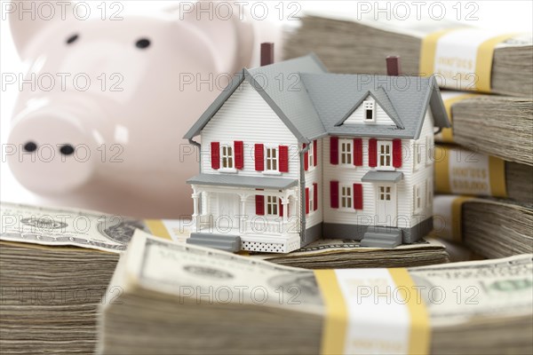 Small house and piggy bank with stacks of hundred dollar bills isolated on a white background