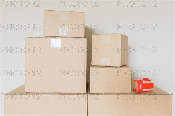 Variety of packed moving boxes and tape gun in empty room against wall