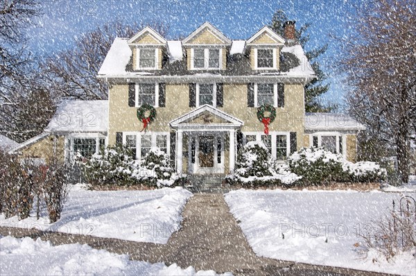 Majestic newly constructed home facade with giant christmas wreaths on a snowing blustery day