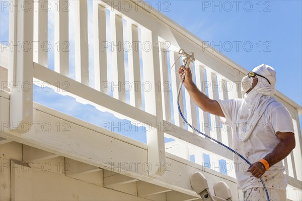 House painter wearing facial protection spray painting A deck of A home