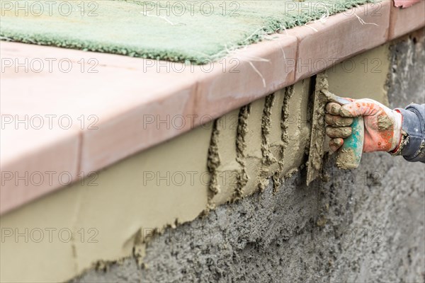 Tile worker applying cement with trowel at pool construction site