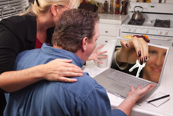 Couple in kitchen using laptop with keys coming through the screen