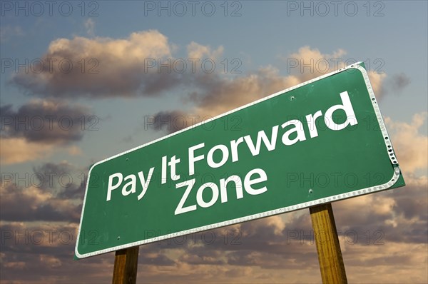 Pay it forward zone green road sign in front of dramatic clouds and sky