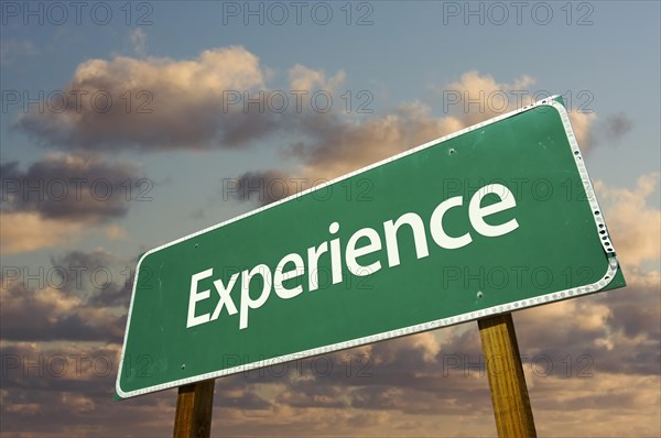 Experience green road sign with dramatic blue sky and clouds