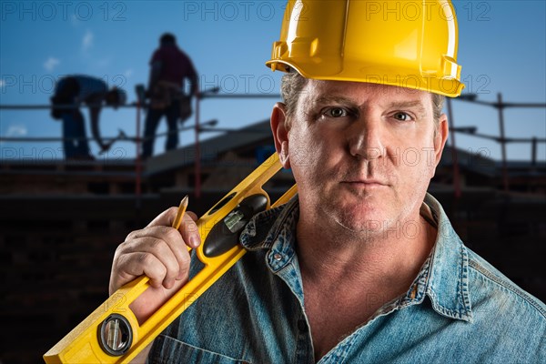 Serious contractor in hard hat holding level and pencil at construction site