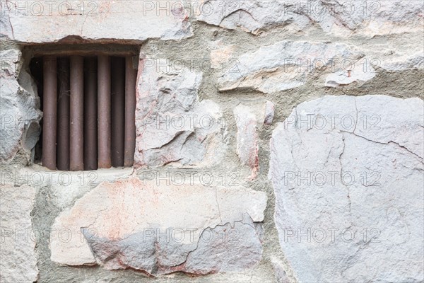 Old stone wall with small iron barred prison cell window