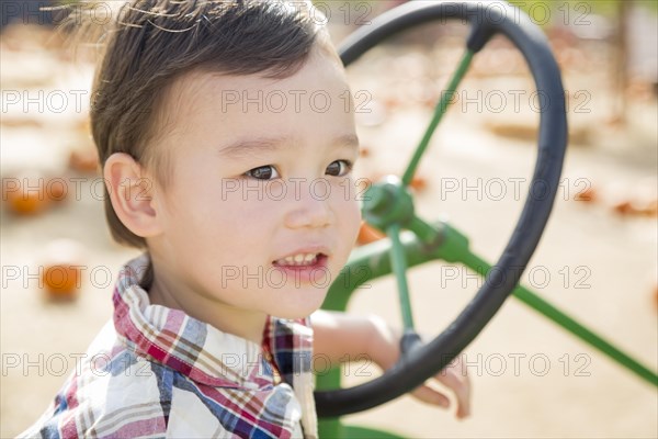 Adorable mixed-race young boy playing on the tractor at the pumpkin patch