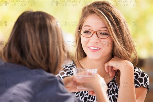 Two mixed-race girlfriends talking over drinks outdoors
