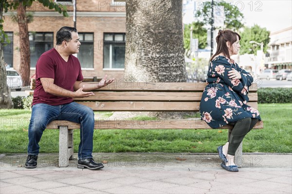 Unhappy mixed-race couple sitting facing away from each other on park bench