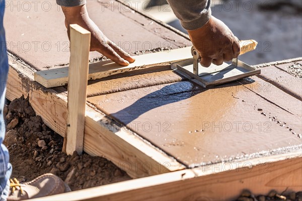 Construction worker using hand groover on wet cement forming coping around new pool