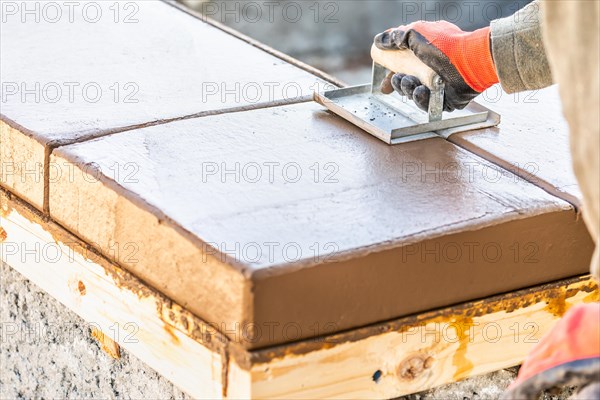 Construction worker using hand groover on wet cement forming coping around new pool